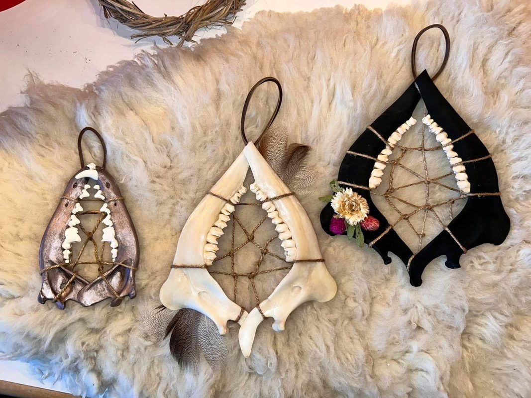 Three animal jawbones strung with cord like dreamcatchers and hung on leather loops, one with a dried flower, on sheepskin.