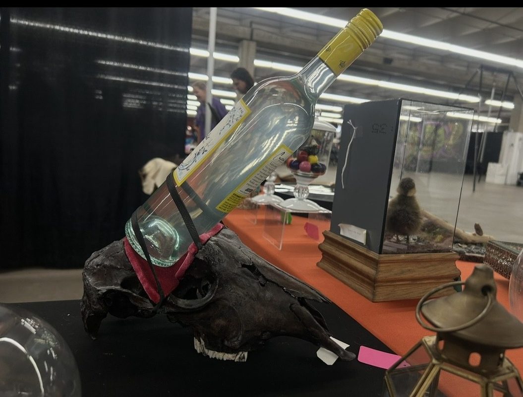 A glass bottle mounted at an angle on a skull, on the booth table at a show.